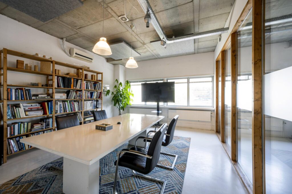 Vergaderruimte aan de Anthony Fokkerweg met een grote tafel, boekenrekken, een flatscreen en industriële plafondafwerking.